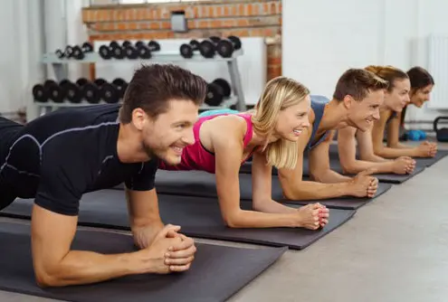 Eine Gruppe von Männern und Frauen führt gemeinsam eine Plank-Übung in einem Fitnesskurs aus, um ihre Kraft und Stabilität des Rückens zu trainieren.