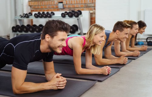 Eine Gruppe von Männern und Frauen führt gemeinsam eine Plank-Übung in einem Fitnesskurs aus, um ihre Kraft und Stabilität des Rückens zu trainieren.