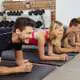 Eine Gruppe von Männern und Frauen führt gemeinsam eine Plank-Übung in einem Fitnesskurs aus, um ihre Kraft und Stabilität des Rückens zu trainieren.