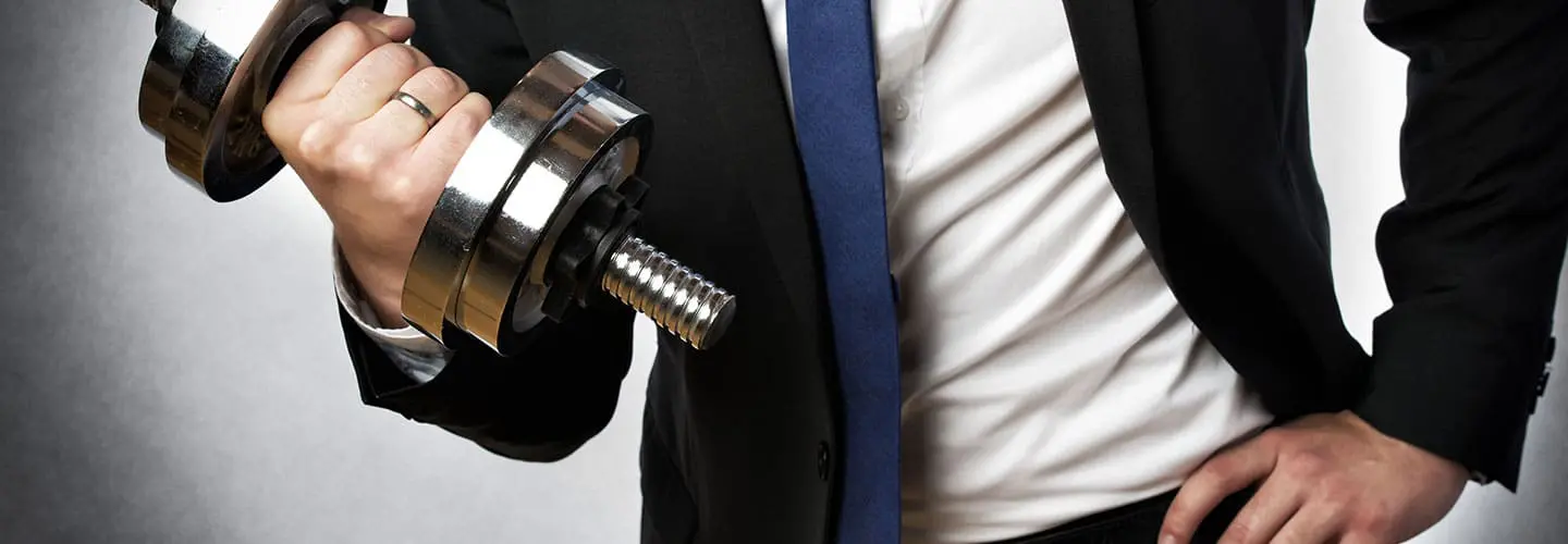 Ein Mann im Anzug hält eine Hantel in der Hand, symbolisiert die Verbindung von körperlicher Fitness und beruflichem Erfolg.
